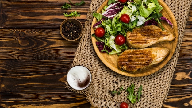 Pfeffer und Bier in der Nähe von Salat und Hühnchen