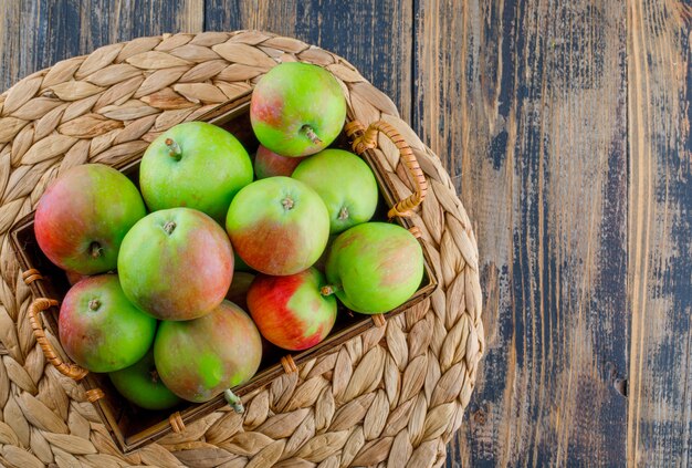 Äpfel in einem Korb auf hölzernem und Weiden-Tischset-Hintergrund. flach liegen.