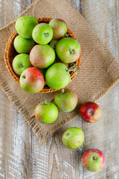 Äpfel in einem Weidenkorb auf Holz und Sack. Draufsicht.