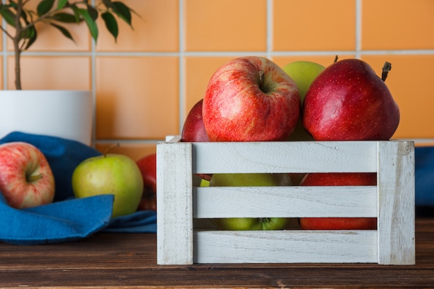 Äpfel in einer weißen Holzkasten-Seitenansicht auf einem hölzernen und orange Fliesenhintergrund
