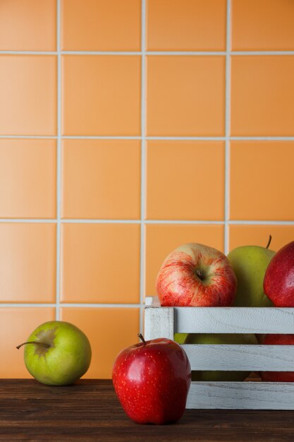 Äpfel in einer weißen Holzkiste auf einem hölzernen und orange Fliesenhintergrund. Seitenansicht.