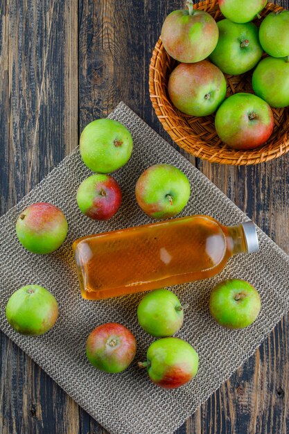 Äpfel mit Getränk in einem Korb auf Holz- und Tischset-Hintergrund, Draufsicht.