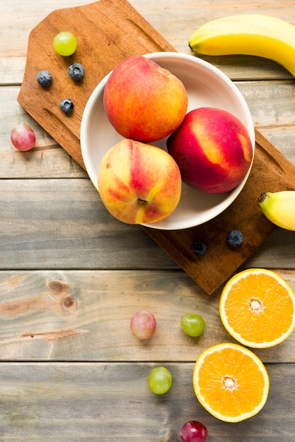 Pfirsich; Äpfel; Trauben; Blaubeeren; Banane und halbierte Orangen auf Schreibtisch aus Holz