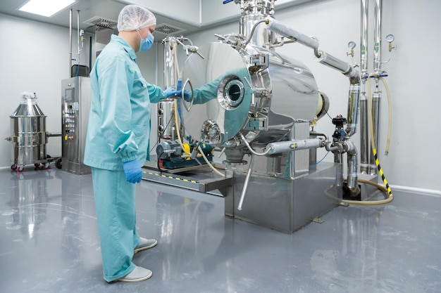 Pharmazeutischer Fabrikarbeiter in Schutzkleidung, der unter sterilen Arbeitsbedingungen an Geräten arbeitet
