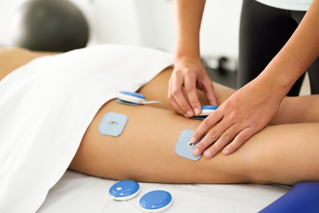 Physiotherapeut, der Elektrostimulation in der Physiotherapie auf ein Bein der jungen Frau anwendet.