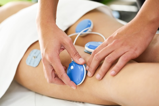 Physiotherapeut, der elektrostimulation in der physiotherapie auf ein bein der jungen frau anwendet.