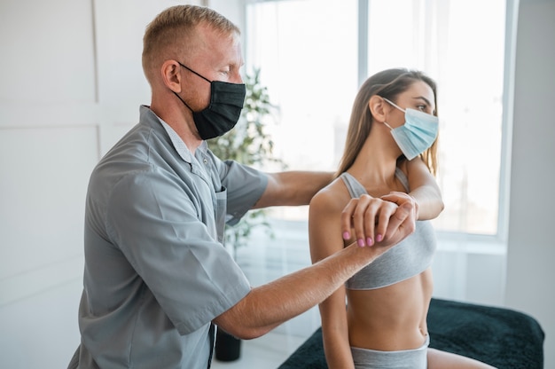 Physiotherapeut trägt medizinische Maske während einer Therapiesitzung mit Patientin