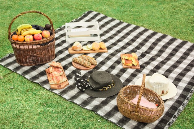 Picknickkorb mit frischen Früchten; Gebackene Brote und Hut auf Decke über dem grünen Gras