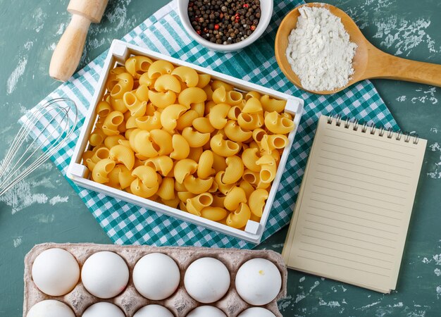 Pipe Rigate Pasta in einer Box mit Eiern, Pfefferkörnern, Stärke, Nudelholz, Schneebesen und Heft