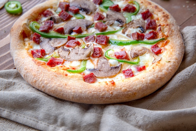 Pizza mit gehackter Wurst, Pilzen und grünem Paprika auf einem Stück Tischdecke