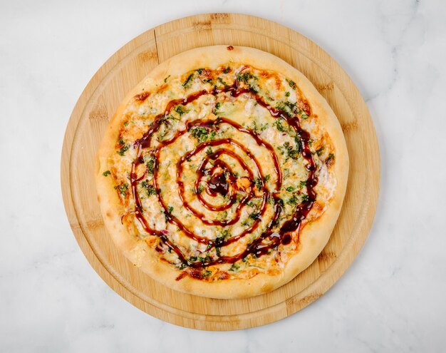 Pizza mit Kräutern und roter Soße auf einer hölzernen Servierplatte.