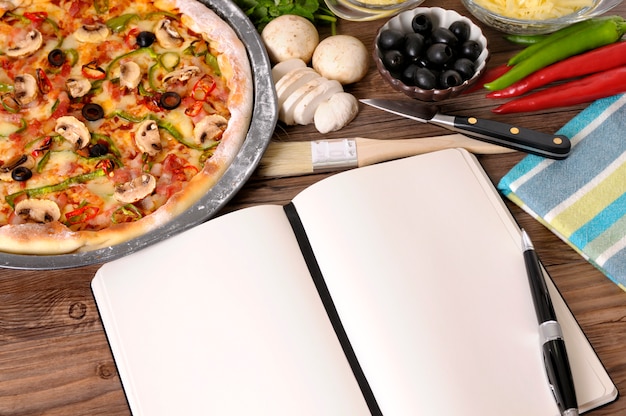 Pizza mit Notebook oder Kochbuch und Zutaten