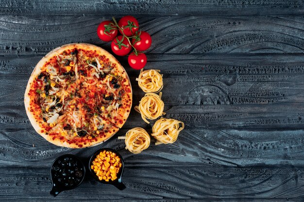 Pizza mit Spaghetti, Tomaten, Oliven, Mais Draufsicht auf einem dunkelblauen Hintergrund