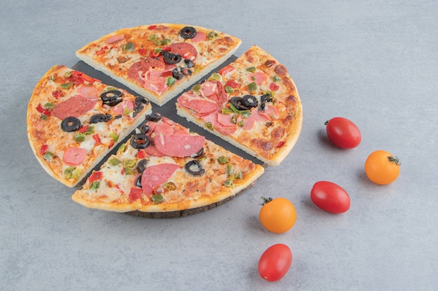 Pizzastücke auf einer Platte neben kleinen Tomaten auf Marmor