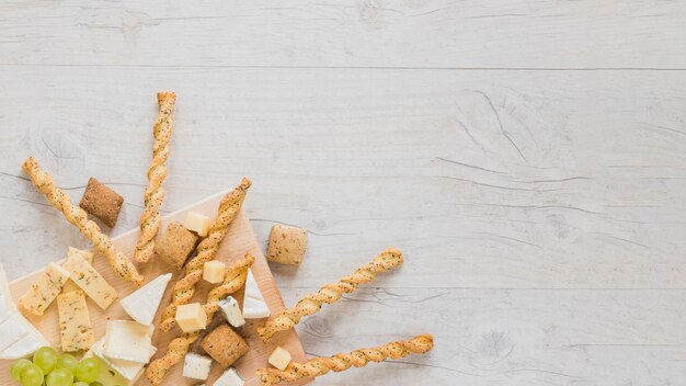 Plätzchen, Brotstangen, Käseblock und Trauben an der Ecke der Holzoberfläche