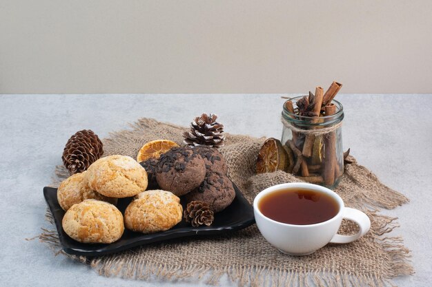 Plätzchenteller, Tee, Zimt und Pinecones auf Leinwand. Foto in hoher Qualität