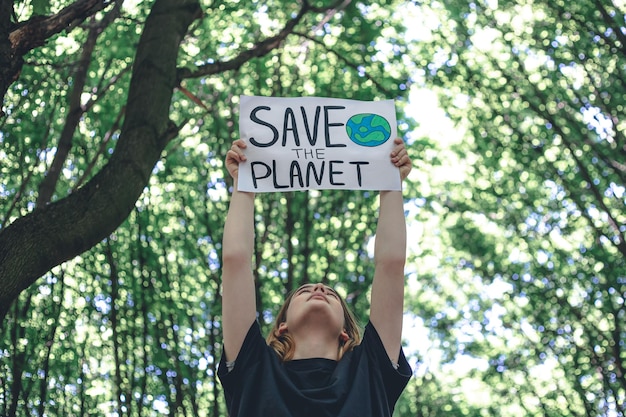 Plakat im Aufruf zur Rettung des Planeten in Frauenhänden im Wald