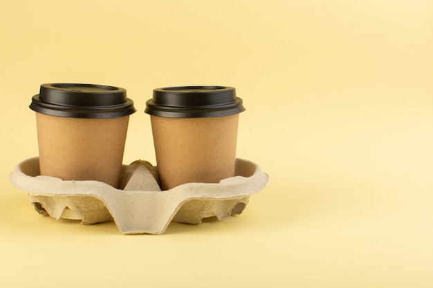 Plastikkaffeetassen der Vorderansicht liefern Kaffeepaar an der gelben Wand