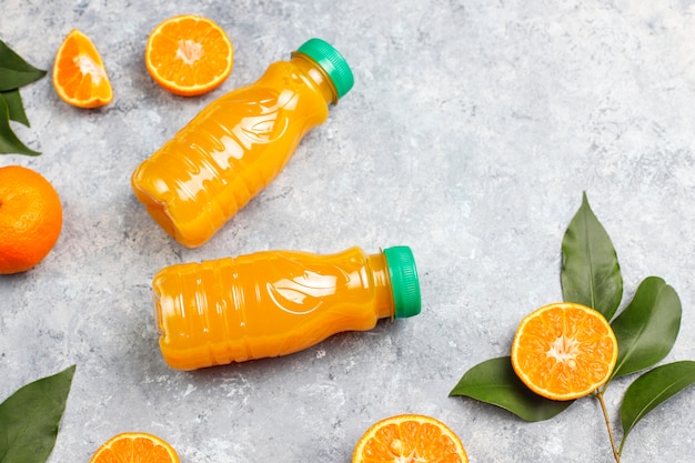 Plastikminiflaschen organischer frischer Orangensaft mit rohen Orangen und Mandarinen
