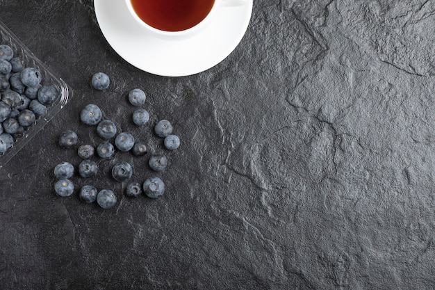 Plastikverpackung mit köstlichen frischen Blaubeeren mit einer Tasse heißem Tee