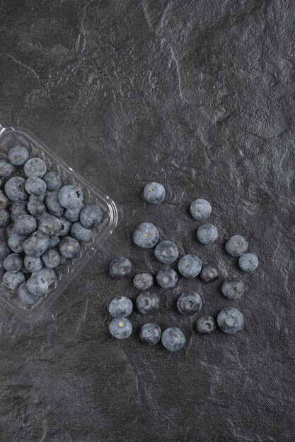 Plastikverpackung mit leckeren frischen Blaubeeren auf schwarzer Oberfläche