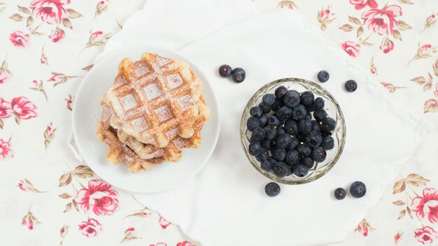 Platte der Waffeln und der Blaubeereschüssel auf Blumenhintergrund