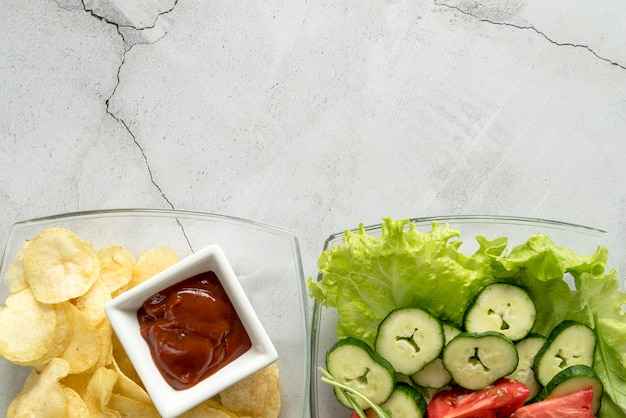 Kostenloses Foto platte des organischen gemüsesalats und der kartoffelchips mit tomatensauce über konkretem hintergrund