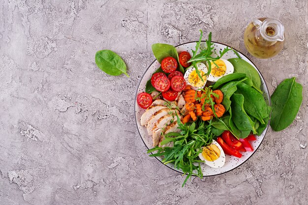Platte mit einem Ketodiätfutter. Kirschtomaten, Hühnerbrust, Eier, Karotten, Salat mit Rucola und Spinat. Keto-Mittagessen. Draufsicht