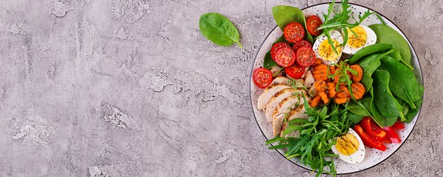 Platte mit einem Ketodiätfutter. Kirschtomaten, Hühnerbrust, Eier, Karotten, Salat mit Rucola und Spinat. Keto-Mittagessen. Draufsicht