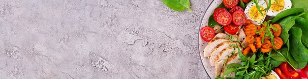 Platte mit einem Ketodiätfutter. Kirschtomaten, Hühnerbrust, Eier, Karotten, Salat mit Rucola und Spinat. Keto-Mittagessen. Panorama-Banner mit Copyspace. Draufsicht