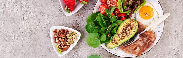 Platte mit einem Ketodiätfutter. Spiegelei, Speck, Avocado, Rucola und Erdbeeren. Keto Frühstück. Draufsicht