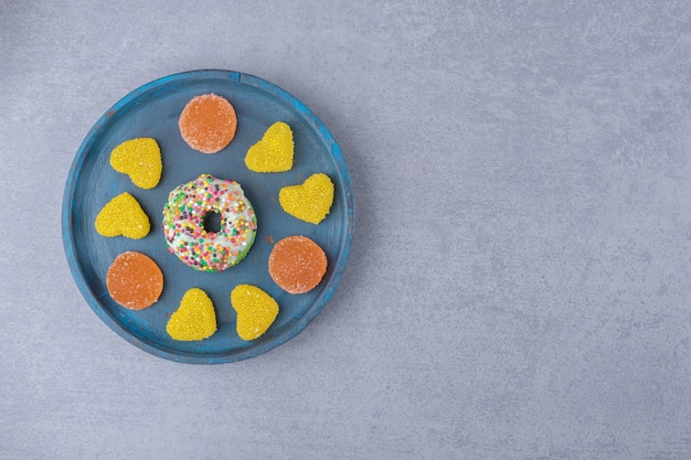 Platte mit einem kleinen Donut und verschiedenen Marmeladen auf Marmoroberfläche