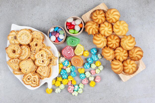 Platte und Tablett voller Kekse mit einem Bündel Süßigkeiten und Marmeladen in der Mitte auf Marmorhintergrund. Hochwertiges Foto
