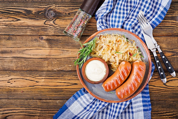 Platte von Würsten und von Sauerkraut auf Holztisch. Traditionelles Oktoberfest-Menü. Flach liegen. Ansicht von oben.