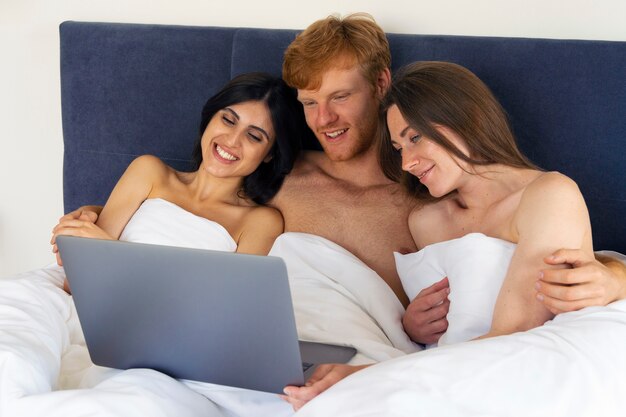 Polyamoröses Paar zu Hause im Bett mit Laptop
