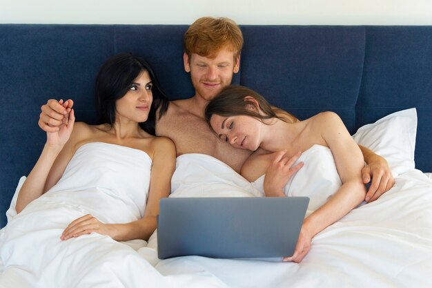 Polyamoröses Paar zu Hause im Bett mit Laptop
