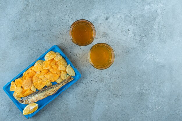 Pommes und Fisch auf einem Holzteller neben zwei Gläsern Bier, auf dem Marmortisch.