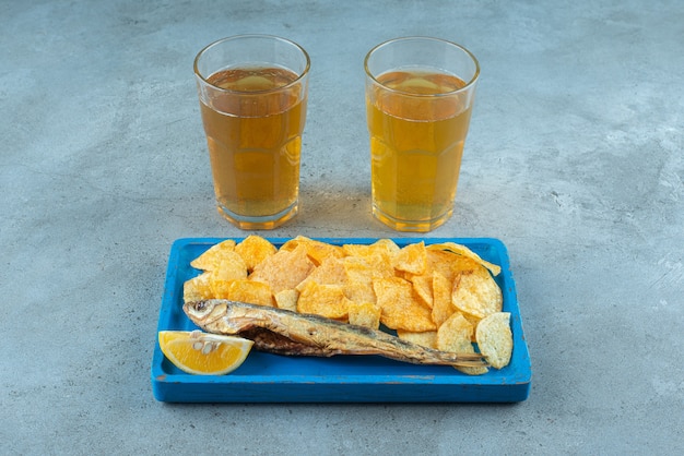 Pommes und fisch auf holzteller neben zwei gläsern bier auf marmor.