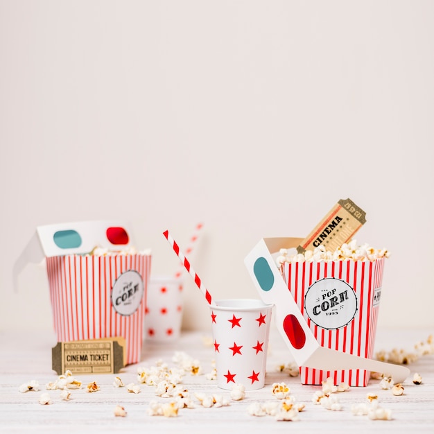 Popcorn; Kinokarte; Einwegglas mit Trinkhalm und Popcorn-Box auf dem Tisch vor weißem Hintergrund