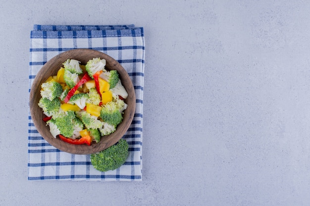Portion Brokkoli- und Pfeffersalat in einer Schüssel auf gefaltetem Handtuch auf Marmorhintergrund. Foto in hoher Qualität