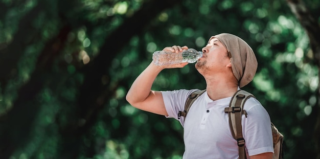 Porträt asiatischer Reisender Mann mit Rucksack Trinkwasser aus Flasche im Wald mit Kopierraum Trinkwasser des männlichen Wanderers im Wald Urlaubs- und Hobbykonzept