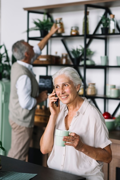 Porträt der älteren Frau sprechend am Handy, der Kaffeetasse hält