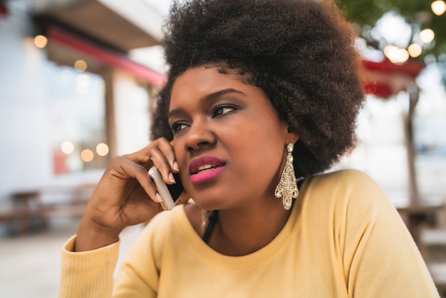 Porträt der afro-lateinamerikanischen Frau, die am Telefon beim Sitzen am Kaffeehaus spricht. Kommunikationskonzept.