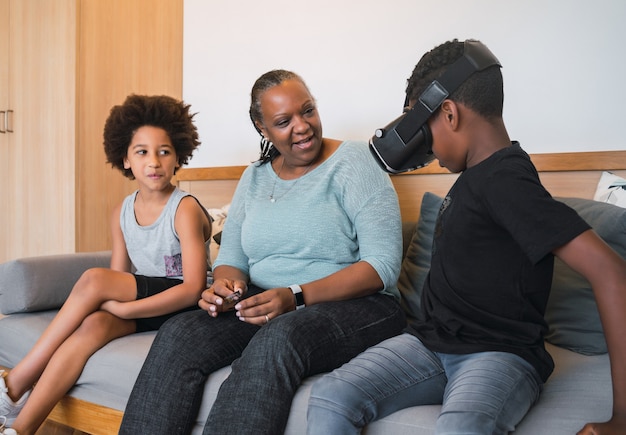 Porträt der afroamerikanischen Großmutter und der Enkelkinder, die zu Hause mit VR-Brille zusammen spielen. Familien- und Technologiekonzept.