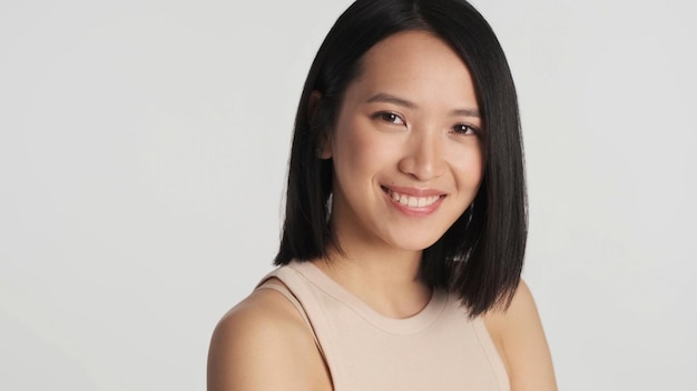 Porträt der asiatischen Frau, die selbstbewusstes Lächeln in die Kamera über weißem Hintergrund sucht Gesichtsausdruck