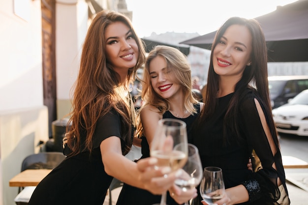 Porträt der atemberaubenden Damen, die das Wochenende mit Gläsern voller Champagner im Vordergrund genießen