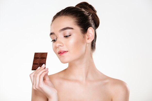 Porträt der attraktiven halbnackten Frau mit dem dunklen Haar Bonbons genießend, die Tafel Milchschokolade essen