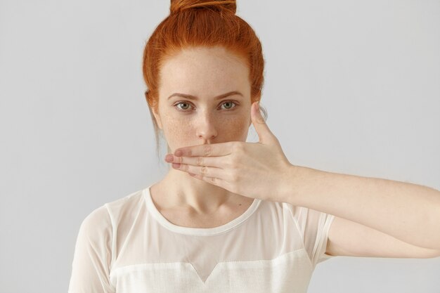 Porträt der attraktiven jungen rothaarigen Frau, die Mund mit Hand bedeckt