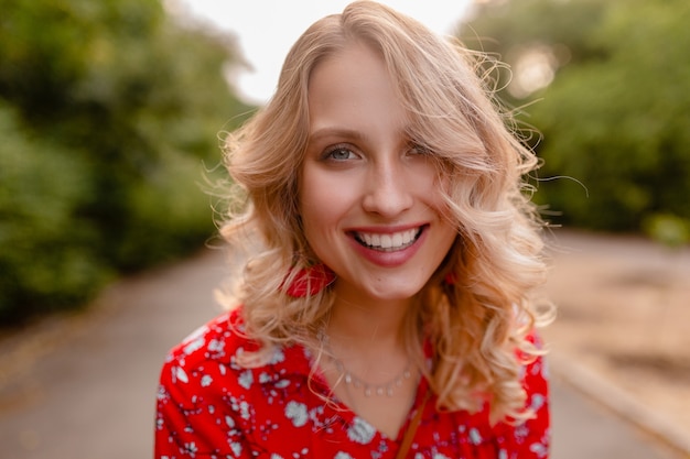 Porträt der attraktiven stilvollen blonden lächelnden Frau im Sommermode-Outfit der roten Bluse, das Ohrringe lächelnd trägt
