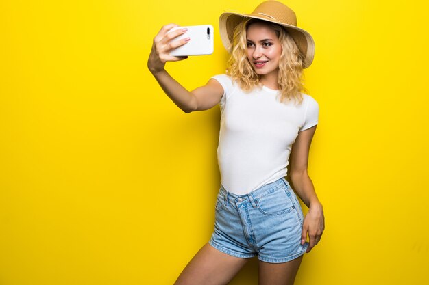 Porträt der aufgeregten Frau, die Spaß hat, während Selfie-Foto lokalisiert über gelbe Wand nimmt